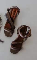 Sandalias de gamuza color azul con taco cuadrado bajo, tiras cruzadas decoradas con flecos de mostacillas y cierre de hebilla en el tobillo.