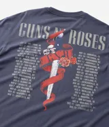 Remera de algodón color gris azulado, con cuello redondo y manga corta. Presenta un estampado gráfico frontal con el logo de la banda Guns N' Roses y calaveras rodeadas de rosas.