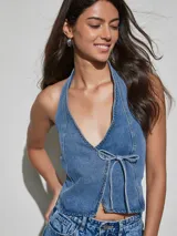 Chaleco de denim azul de corte ajustado, con escote halter pronunciado, detalle de tachas metálicas en los bordes y cierre delantero con tiras para anudar.