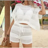 Conjunto de dos piezas tejido en punto calado color blanco, compuesto por una blusa de corte holgado con cuello redondo y mangas cortas, y un short de tiro medio con cintura elástica ajustable mediante cordón.