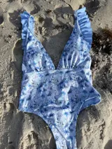 Traje de baño entero con estampado floral en tonos celeste y azul, escote en V pronunciado, breteles con volados y corte colaless.