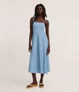 Vestido midi de denim ligero y lino, color celeste, con escote recto, tirantes finos con lazo ajustable en los hombros, busto estructurado con recortes y falda evasé de corte midi.