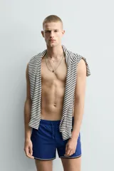 Short de baño azul con cintura elástica ajustable con cordón, bolsillos laterales y ribetes en contraste en los bordes.