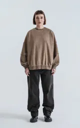 Buzo de cuello redondo color marrón claro, confeccionado en algodón premium con textura acanalada. Presenta costuras expuestas y detalles deshilachados en cuello, puños y ruedo, con un calce oversize y mangas abullonadas.