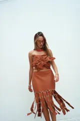 Falda midi de cuero color suela, con diseño de tiras verticales unidas por argollas metálicas en el ruedo, creando un efecto de flecos estructurados.