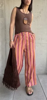 Pantalón de lino a rayas verticales en tonos rojo, naranja, marrón y rosa, con cierre y botón, y dos bolsillos laterales.