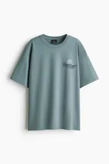Remera de algodón verde militar, de corte holgado, con cuello redondo y mangas cortas. Cuenta con un pequeño estampado gráfico con texto en el pecho.