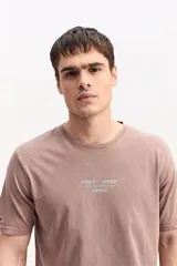 Remera de algodón color marrón con efecto gastado, de manga corta, cuello redondo y estampa tipográfica sutil al frente.