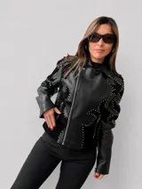 Chaqueta tipo biker de eco cuero negro con diseño estructurado. Presenta apliques de tachas metálicas en formas orgánicas sobre paneles de gamuza sintética, cierre frontal metálico y bolsillos laterales con cierre.
