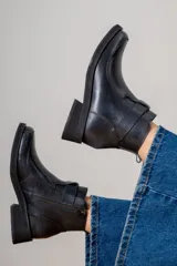 Bota corta de cuero con textura granulada, diseño de caña media con detalle de tira envolvente en el tobillo y cierre lateral metálico. Cuenta con suela plana y taco cuadrado bajo.