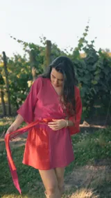 Top cruzado de muselina con diseño bicolor en tonos fucsia y rojo, de manga corta amplia y lazo ajustable en la cintura.