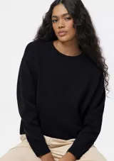 Buzo de punto negro con cuello redondo acanalado, mangas largas con puños ajustados y diseño holgado.
