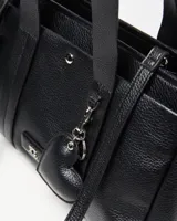 Cartera de mano de cuero sintético negro con textura granulada, doble asa superior, detalle de llavero en forma de corazón y placa metálica frontal con el logo de la marca.
