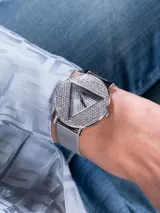 Reloj analógico Guess con caja redonda de 36 mm y malla de acero inoxidable tipo milanesa en tono plateado. La esfera presenta un diseño triangular central rodeado de cristales brillantes.