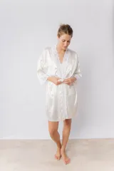 Bata kimono de satén elastizado color blanco, con puntilla en la delantera y en las mangas. Las mangas son al codo y el largo de la bata es por encima de la rodilla. Incluye un lazo de satén para ajustar en la cintura.