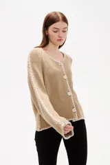 Cardigan de punto color natural, con cuello en V, cierre frontal con botones y diseño holgado. Presenta detalles de costuras decorativas bordadas a lo largo de las mangas y en los bordes.