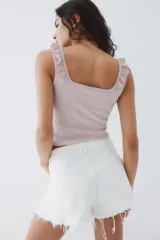 Musculosa corta de ajuste entallado en punto acanalado, color rosado pálido. Presenta escote cuadrado con un ribete de volado fruncido que se extiende sobre los breteles.