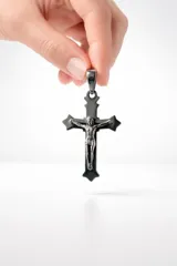 Dije de acero con forma de cruz, con diseño de crucifijo en relieve en tono plateado sobre una base de cruz negra.