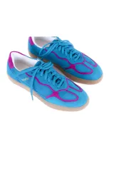 Championes de estilo deportivo vintage, confeccionados en cuero vacuno y gamuza. Presentan una combinación de colores azul vibrante con detalles en fucsia intenso, suela plana de goma en tono neutro y logo de la marca grabado en dorado en el lateral.