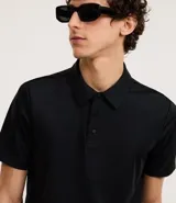 Camisa polo masculina de manga corta, confeccionada en tejido técnico de poliamida con elastano. Presenta cuello inglés con tapeta de tres botones, ofreciendo propiedades de secado rápido, elasticidad y confort térmico.