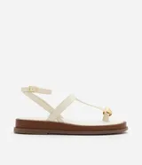 Sandalia plana tipo salomé color beige, con tiras finas, cierre con hebilla lateral y detalle decorativo dorado en la parte frontal. Cuenta con una suela de plataforma baja en tono madera.