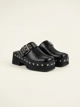 Zueco de cuero encerado color negro, con diseño de punta cuadrada, detalle de tachas metálicas en el lateral y hebilla ajustable en la capellada. Cuenta con suela de goma.