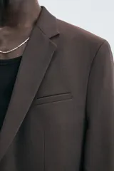 Blazer de corte regular fit confeccionado en tejido con lana. Presenta cuello con solapas de muesca, cierre frontal de un botón, bolsillos de vivo en el pecho y en la cadera, y aberturas en la espalda.