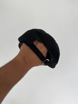 Gorro tipo gorra de béisbol color negro con visera curva. Presenta un bordado frontal de un macetero con flores de colores (rosa, azul, rojo y naranja) y el texto "OLIVER'S FLOWER GARDEN" en blanco sobre un fondo verde.