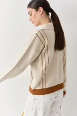 Buzo de punto color beige con rayas verticales marrones, cuello polo con cierre frontal, puños y ruedo acanalados en color marrón, y cordones amarillos ajustables en la cintura.