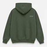 Canguro con capucha de calce oversize, confeccionado en tejido pesado color gris claro. Presenta un bordado minimalista con la palabra 'ASCEND' en la parte superior trasera, puños y ruedo acanalados.