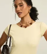 Vestido corto color amarillo pálido, con escote redondo y mangas cortas. Presenta recortes verticales en el torso que definen la silueta y una falda ligeramente acampanada.