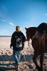 Hoodie oversize negro con capucha, con gran estampado blanco en la espalda que presenta un diseño de palmera dentro de un marco a cuadros y texto.