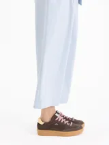 Zapatilla de cuero descarne color rosa, con suela de caucho color caramelo. Presenta cordones oscuros con un aplique de cristal decorativo y detalle de cuero liso en el talón.