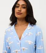 Pijama largo estilo americano de poliéster, compuesto por una camisa de manga larga con cuello solapa y cierre frontal de botones, y un pantalón largo de corte recto. Presenta un estampado integral del personaje Cinnamoroll sobre un fondo celeste.
