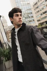 Camisa de corte boxy con estampado de cuadros pequeños en tonos oscuros. Presenta cuello camisero en color negro, cierre frontal con botones, canesú en la parte superior y un bolsillo en el pecho con etiqueta de la marca Kapsul Studio.
