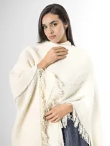 Ruana confeccionada en tejido de punto color off white, con diseño amplio y flecos en los bordes.