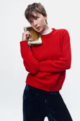 Cartera pequeña color dorado metálico con cierre superior. Presenta tachas plateadas decorativas a lo largo de los bordes superior e inferior.