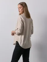 Blusa de manga larga con escote en V, confeccionada en tejido ligero con estampado de rayas verticales en tonos beige y blanco. Presenta un diseño con pliegue frontal y mangas ajustables mediante presilla y botón.