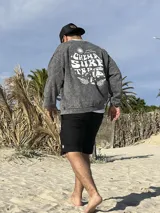 Buzo gris con efecto lavado, cuello redondo y puños acanalados. Estampado en el frente con la frase "Chema Surf Trip" y un dibujo de una camioneta combi.