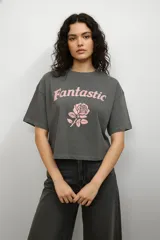Remera de algodón color gris topo, de corte holgado y diseño cropped. Presenta cuello redondo y una estampa frontal con forma de corazón, mariposa y texto decorativo.