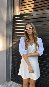 Vestido corto color crudo, con escote en V y mangas 3/4 abullonadas con detalles de calado.