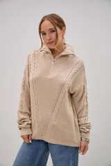 Sweater de punto color beige con cuello polo y cierre frontal parcial. Presenta un diseño con texturas combinadas, incluyendo detalles de trenzas en los laterales y un panel central con textura de relieve, mangas largas con puños ajustados.