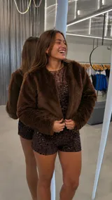 Chaqueta corta de piel sintética en color marrón, de textura suave y mullida, con mangas largas y diseño abierto sin cierre frontal.