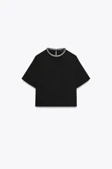 Remera negra de corte recto y holgado, con cuello redondo decorado con apliques de brillos y mangas cortas. Presenta una abertura en la espalda con cierre de botón oculto.