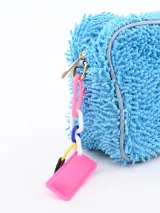 Necessaire de textura tipo felpa o chenille en color celeste, con cierre perimetral y etiqueta frontal de la marca Common Wear. Incluye un detalle de cadena plástica multicolor con una placa rosa colgante en el lateral.