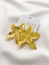 Aros colgantes dorados con forma de flor y textura irregular con pequeñas esferas.