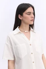 Camisa de manga corta color rosado, con cuello camisero, cierre frontal con botones y dos bolsillos delanteros con solapa. Presenta un corte corto y holgado, con dobladillo redondeado.