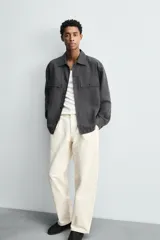 Pantalón de corte regular fit confeccionado en tejido de algodón con textura de espiga. Presenta cintura con pliegues frontales, bolsillos laterales y bolsillos traseros de vivo con botón. Cierre frontal con cremallera y botón.