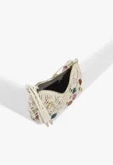 Cartera baguette de cuero color beige con diseño trenzado tipo red y apliques de cuentas de colores y formas metálicas en el cuerpo y en la manija. Cuenta con cierre superior y etiqueta colgante de la marca.