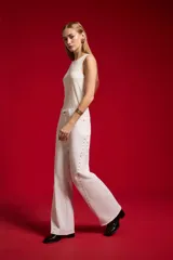 Pantalón jean blanco de corte flare y tiro alto, con detalles de tachas a lo largo de las costuras laterales y botamanga sin costura.